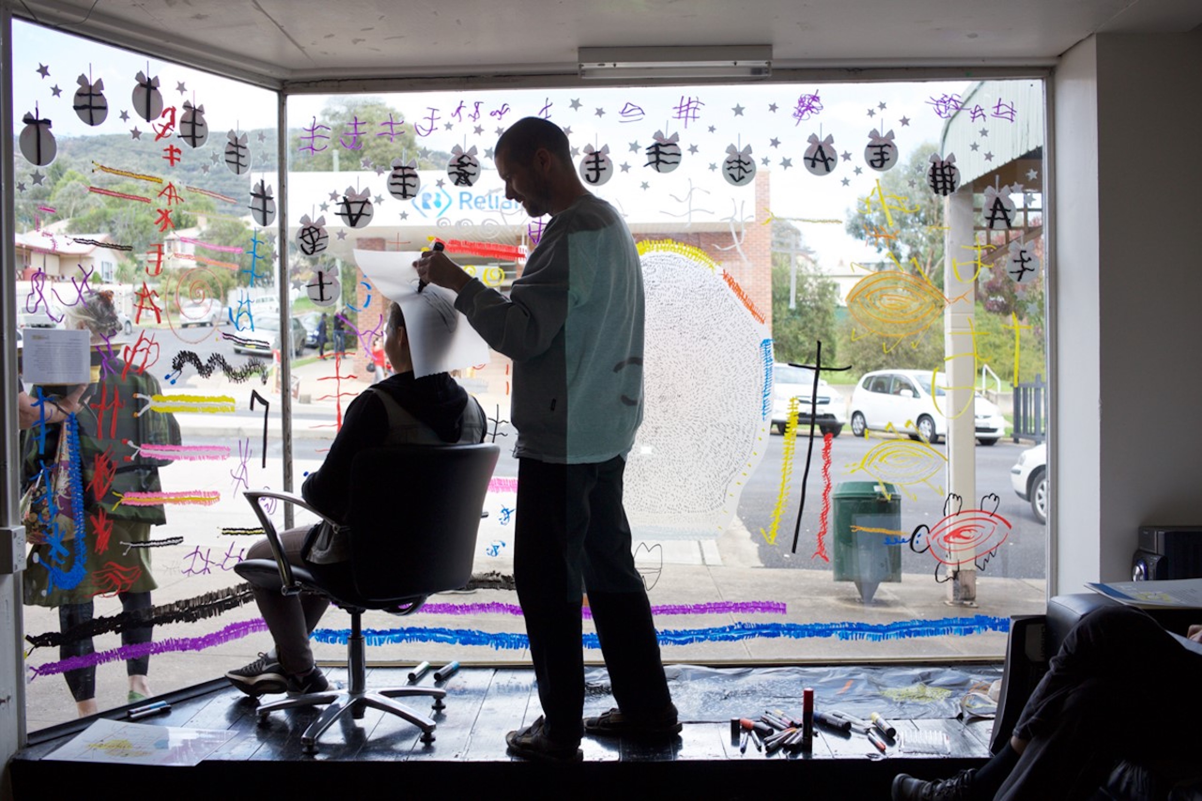 An artist stands in a display window reading/drawing the crown of a person's head.